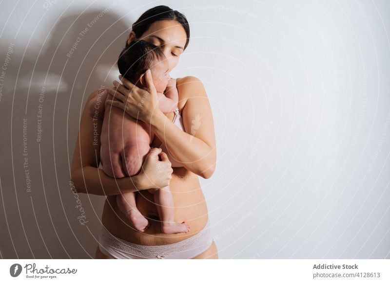 Mutter hält kleines Baby auf Händen im Zimmer Frau Liebe Kuss Dessous Umarmen Zusammensein Angebot sanft Unterwäsche Pflege Kind Mutterschaft jung Glück