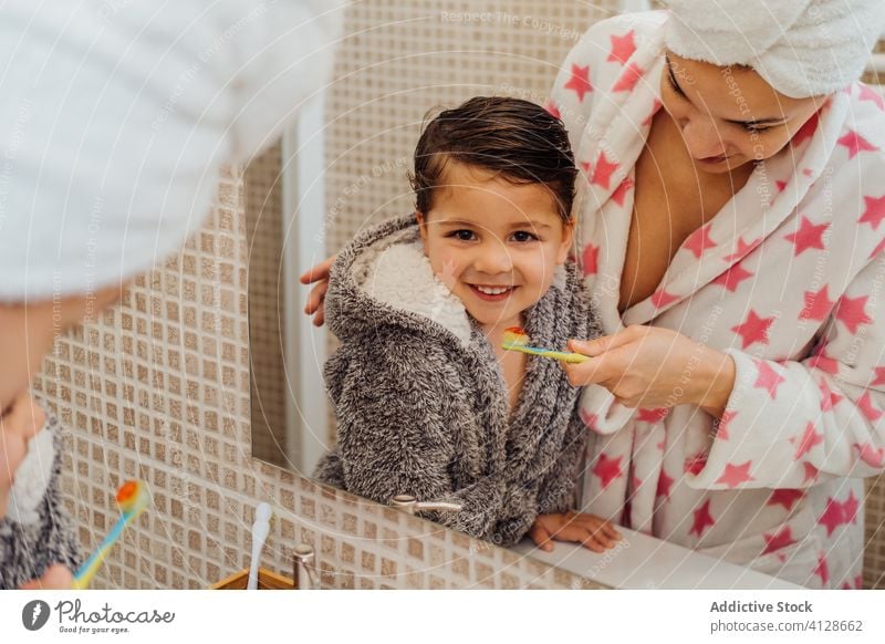 Fröhlicher Sohn und Mutter mit Zahnbürste im Badezimmer Bürste Zähne Junge Bademantel mündlich Hygiene Lächeln wenig Kind Mama Elternschaft Gesundheit Spiegel