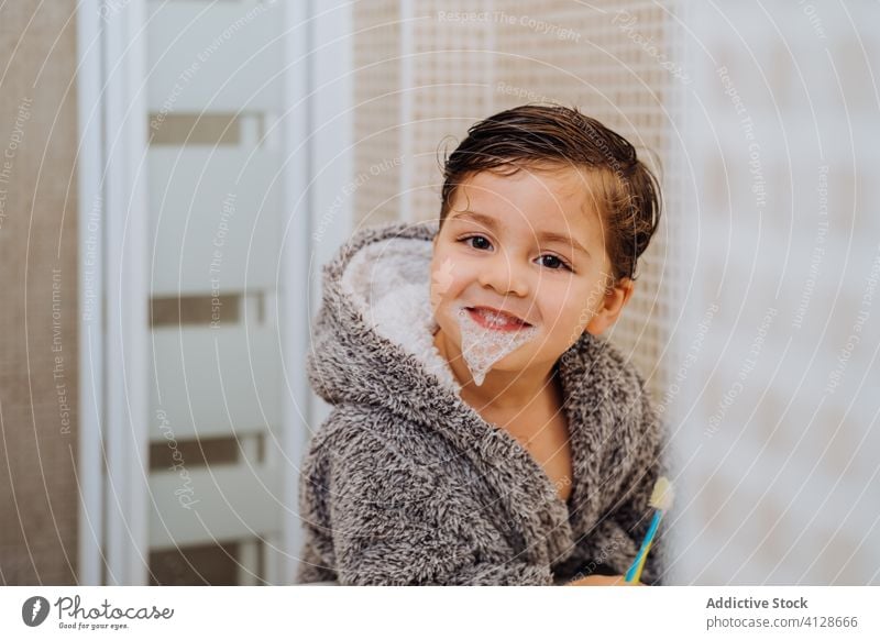 Kleiner Junge beim Zähneputzen im Badezimmer Bürste Zahnbürste wenig Kind Lächeln Bademantel mündlich Hygiene nasses Haar heiter weich gemütlich Komfort