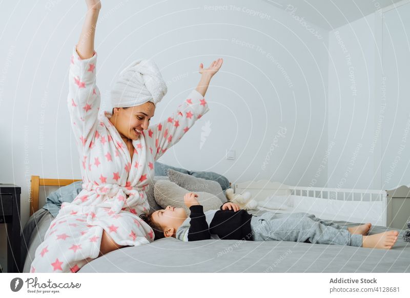 Zufriedene Mutter spielt mit Kind im Schlafzimmer spielen Sohn Spaß haben Zusammensein wenig verkleidend Spiel Inhalt Bademantel Zeitvertreib Junge Eltern
