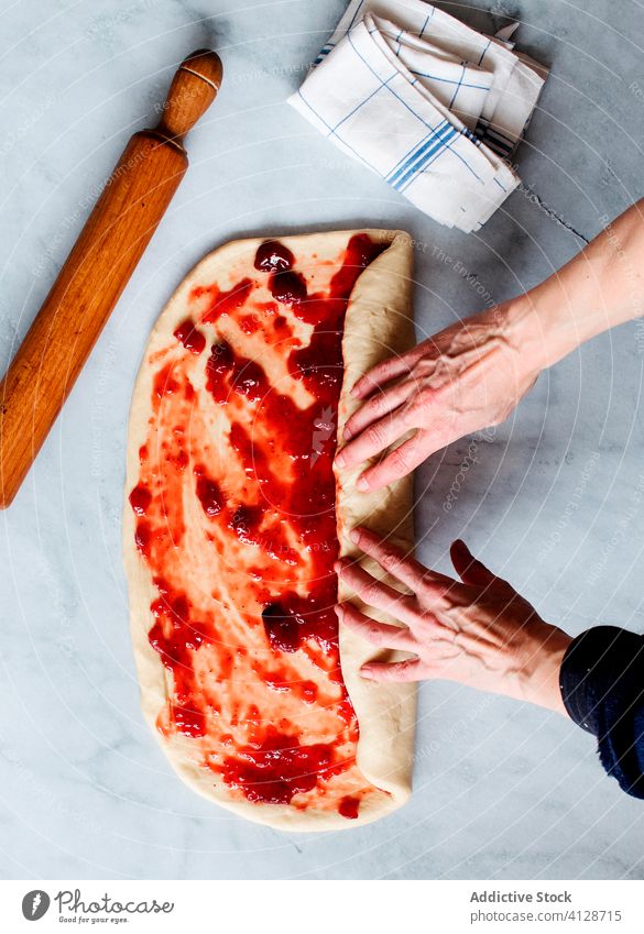 Anonyme Person, die frische Erdbeerbrioche auf einem Marmortisch herstellt Frucht Erdbeeren bewahren Hände Butter Mehl Brotbelag Gebäck Süße Lebensmittel Zucker