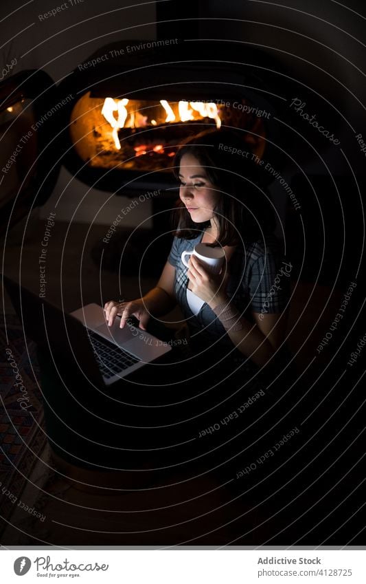 Frau mit Laptop im dunklen Wohnzimmer am Kamin Feuerstelle Browsen Kälte Wochenende Inhalt benutzend Netbook dunkel Lächeln heiter froh sitzen Stock Tasse
