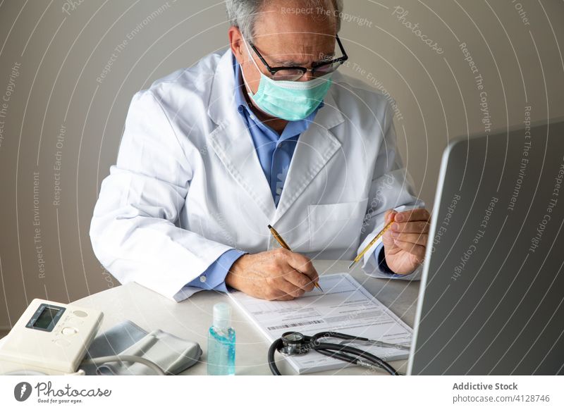 Älterer männlicher Arzt, der nach der Untersuchung eines Patienten einen medizinischen Bericht ausfüllt besetzen Mann gealtert Thermometer Temperatur Virus