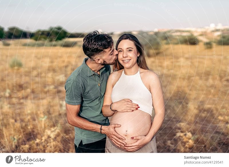 Junge schwangere Frau und ihr Ehemann Partnerschaft Porträt Küssen Warten in die Kamera schauen Landschaft Glück Lächeln außerhalb im Freien Umarmung Magen