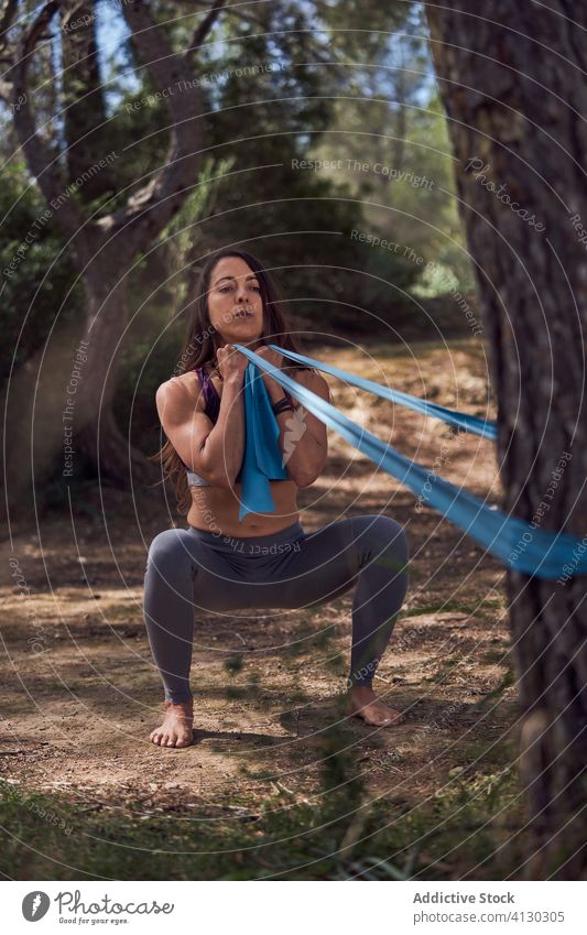 Seitenansicht einer Sportlerin beim Training mit Gummiband im Park Übung Dehnung Band Kniebeuge elastisch Herz widersetzen Seil Fitness Fixierung Gesundheit