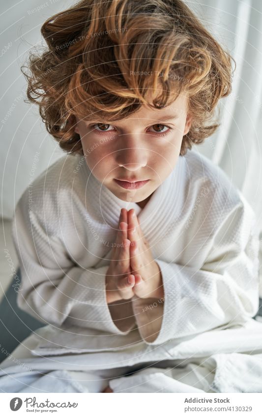 Konzentrierter Junge im weißen Kimono beim Meditieren üben meditieren Judo Kind heimwärts in die Kamera schauen Beine gekreuzt Hände zusammen Übung Windstille