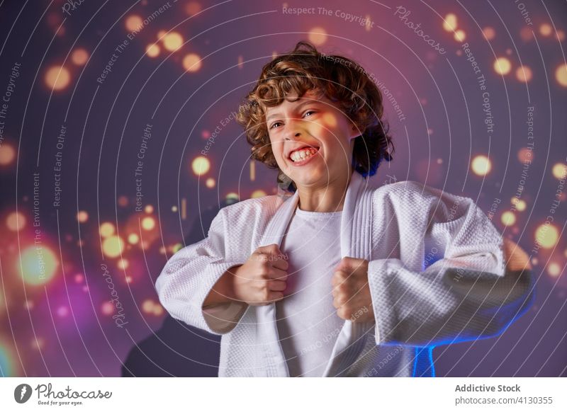 Aufgeregter Junge in weißem Kimono, der inmitten glühender Lichter schreit schreien Kraft Judo stark attackieren üben kämpferisch Kunst Sport Raum expressiv
