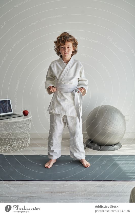 Junge in weißem Kimono lernt zu Hause am Laptop Judo jung online Tutorial heimwärts positionieren lernen üben Training Kindheit Aktivität krause Haare Computer
