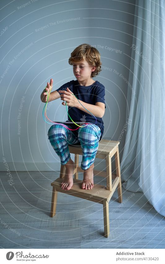 Kind mit Tablette lernt Katzenwiege-Spiel Schnur spielen lernen Wiege Kreativität Figur Hocker Pyjama heimwärts Junge Fokus Krawatte Vorstellungskraft Fähigkeit