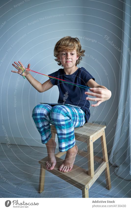 Junge spielt Denksportaufgabe mit Schnur Kind Spiel spielen Tablette lernen Wiege Kreativität Figur Hocker Katze Pyjama heimwärts Fokus Vorstellungskraft
