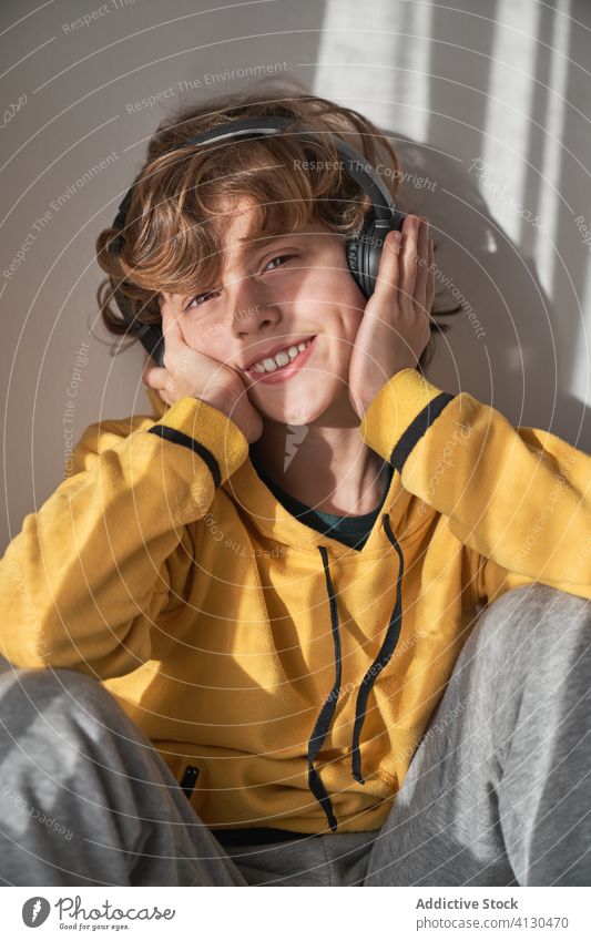 Glücklicher sorgloser kleiner Junge mit Kopfhörern, der seine Lieblingsmusik in einem hellen, modernen Raum genießt Musik allein träumen genießen Gesang