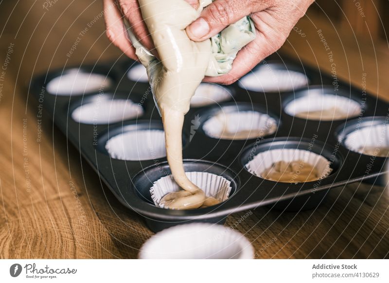 Ältere Hausfrau gießt Teig in Muffinförmchen eingießen Teigwaren Muffin-Gehäuse besetzen Tablett Küche Senior Frau heimwärts Konditor Koch vorbereiten Papier