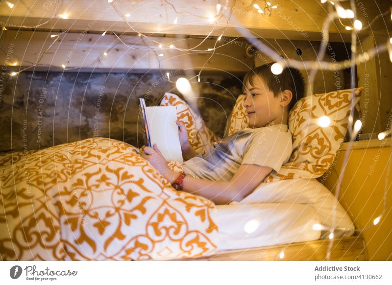Kind schaut Tablette im Bett mit Girlande dekoriert Junge benutzend gemütlich Komfort zuschauen Video Kälte Freizeit heimwärts Abend glühen leuchten