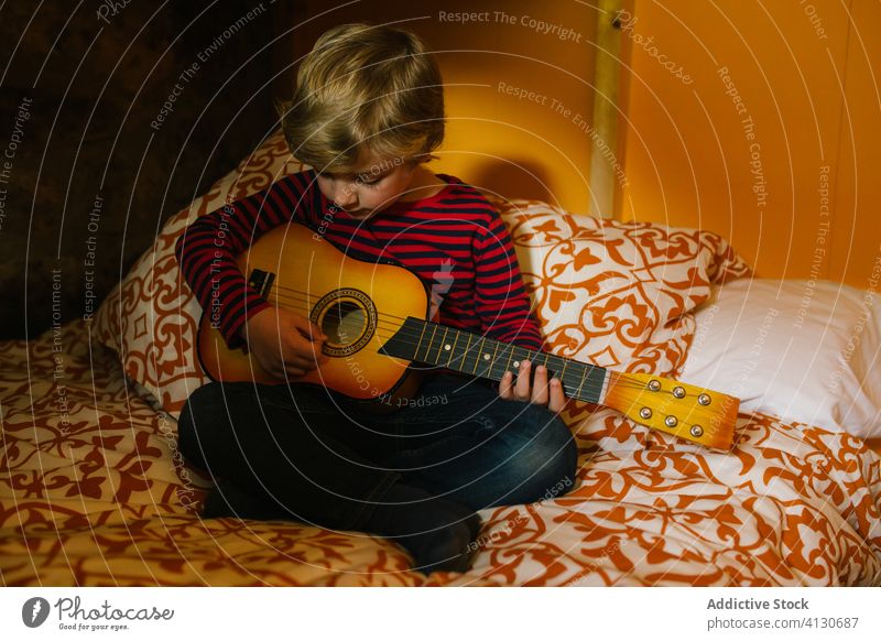 Ruhiger Junge spielt Gitarre auf dem Bett spielen Ukulele Kind Kälte Komfort Spaß haben Hobby Kantabrien Spanien Kindheit lässig Outfit sitzen
