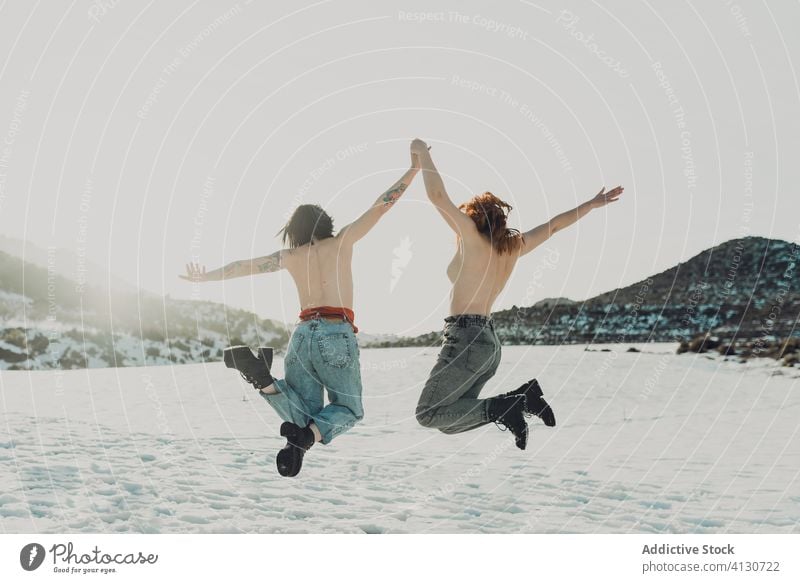 Glückliche barbusige Frauen, die in einem verschneiten Feld springen oben ohne Freundin sorgenfrei Freiheit genießen Schnee Zusammensein Paar Winter Natur
