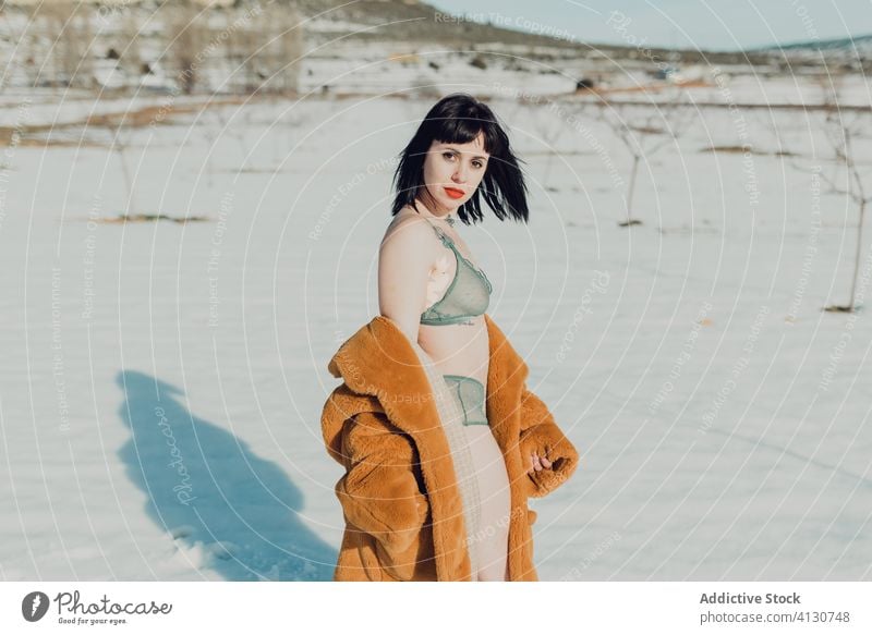 Junge Frau in Pelzmantel und Dessous steht im verschneiten Feld sinnlich Schnee Natur Winter Mantel brünett selbstbewusst trendy jung schlank Stil Mode Dame