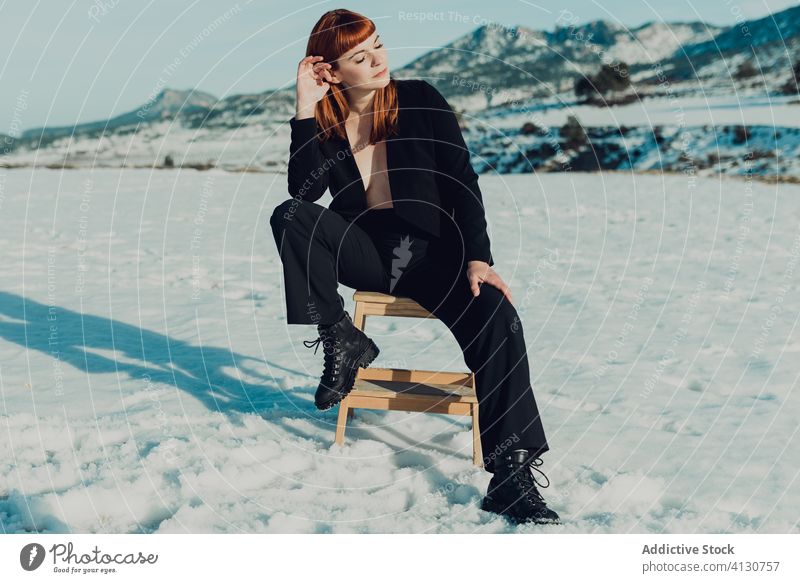 Trendy Frau in schwarzem Anzug sitzt in verschneiten Feld trendy Stil Mode selbstbewusst modern Natur Schnee nackte Brust unabhängig formal sitzen Dame jung