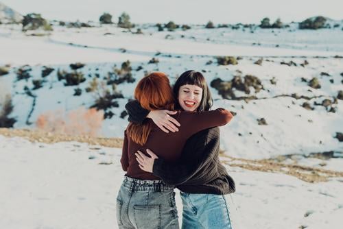 Glückliche Frauen umarmen sich auf einem verschneiten Feld Umarmen Umarmung Freund heiter Zusammensein Schnee Winter Natur Landschaft lässig Freundin Lächeln