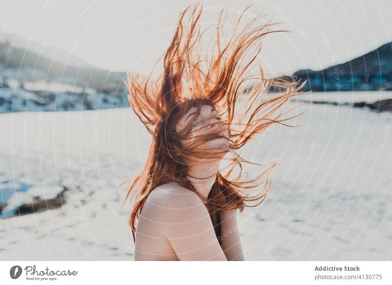 Junge Frau mit im Wind wehenden Haaren in einem verschneiten Feld stehend rote Haare oben ohne Winter fliegendes Haar Natur Glück Schnee sich[Akk] entspannen