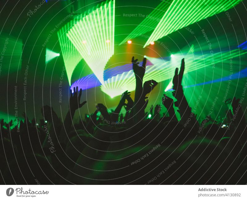 Menschen mit erhobenen Armen während der Show zeigen Konzert ausführen Menge Publikum Arme hochgezogen Silhouette Schauplatz leuchten blau grün neonfarbig Musik