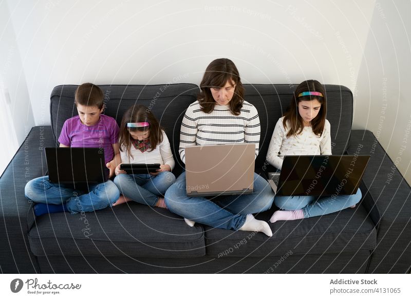 Seriöse Mutter und Kinder verbringen zu Hause Zeit miteinander, indem sie Gadgets auf dem Sofa benutzen Laptop beschäftigt Süchtige benutzend heimwärts