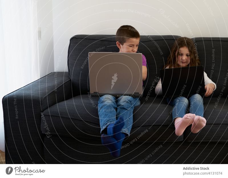 Gruppe von Kindern, die zu Hause auf dem Sofa sitzend Laptops benutzen heimwärts benutzend Zusammensein Menschengruppe Raum Komfort Internet Freundschaft