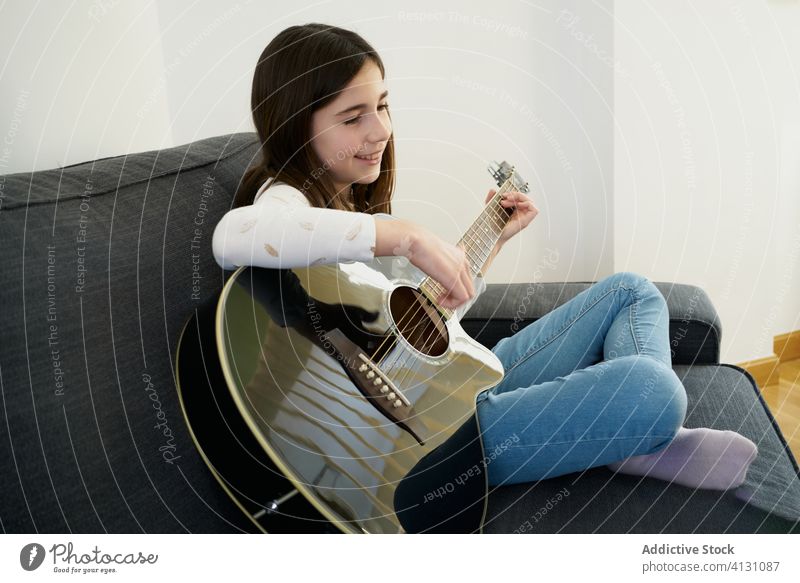 Junges lächelndes Mädchen spielt akustische Gitarre auf dem Sofa zu Hause heimwärts spielen jung heiter Beine gekreuzt sich[Akk] entspannen Instrument Freude