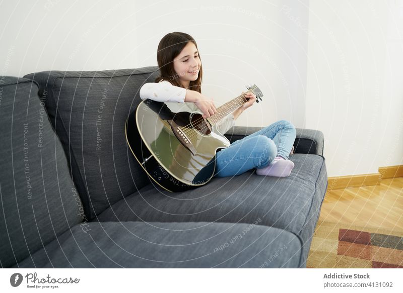 Junges Mädchen, das seiner Schwester auf dem Sofa das Gitarrenspiel beibringt Kinder Zusammensein spielen lehren lernen erklären Geschwisterkind akustisch Hobby