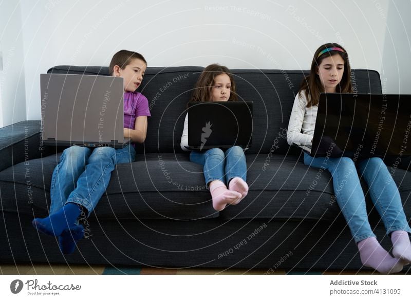 Gruppe von Kindern, die zu Hause auf dem Sofa sitzend Laptops benutzen heimwärts benutzend Zusammensein Menschengruppe Raum Komfort Internet Freundschaft