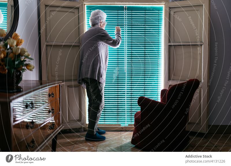 Ältere Frau schaut während der Coronavirus-Quarantäne aus dem Fenster Aufenthalt heimwärts Senior einsam Mundschutz verhindern behüten allein Einsamkeit