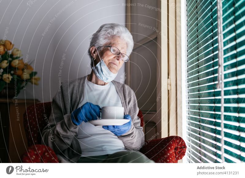 Ältere Frau mit einer Tasse Tee, die während der Quarantäne zu Hause bleibt Coronavirus Aufenthalt heimwärts Senior trinken Fenster einsam traurig besinnlich