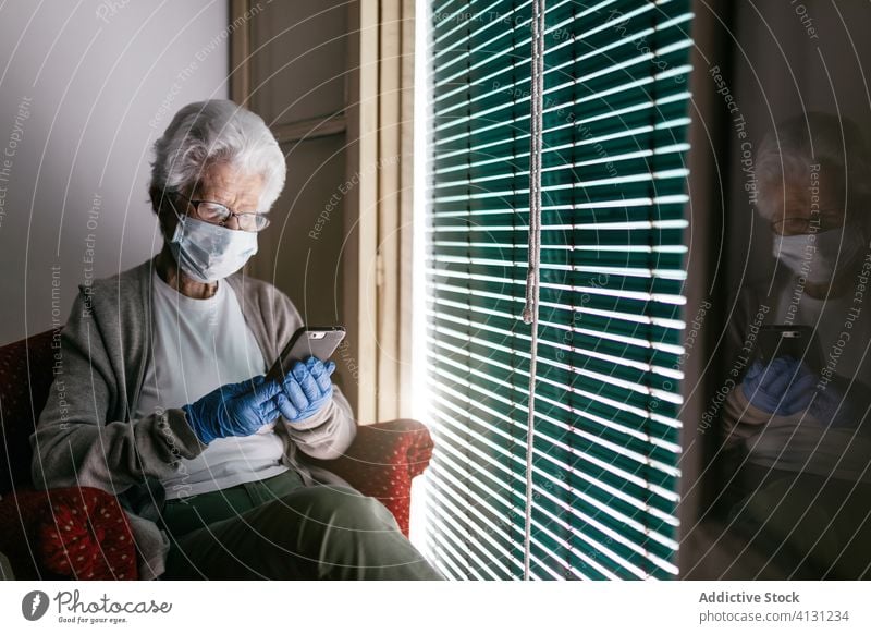 Ältere Frau, die während der Selbstisolierung zu Hause mit ihrem Smartphone chattet Aufenthalt heimwärts Coronavirus Senior Fenster benutzend Kommunizieren
