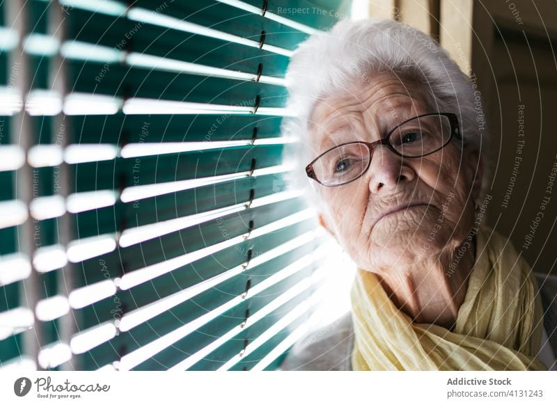 Ältere Frau steht während der Pandemie am Fenster Senior Coronavirus Aufenthalt heimwärts einsam unglücklich traurig Fensterladen besinnlich Quarantäne