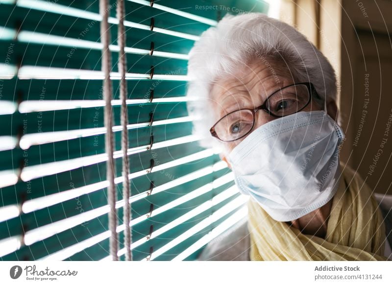Ältere Frau steht während der Pandemie am Fenster Senior Coronavirus Aufenthalt heimwärts einsam unglücklich traurig Fensterladen besinnlich Quarantäne