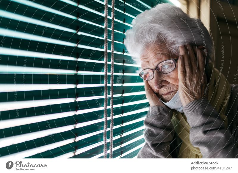 Besorgte ältere Frau steht während der Pandemie am Fenster Senior Coronavirus Aufenthalt heimwärts einsam unglücklich traurig Fensterladen besinnlich Quarantäne