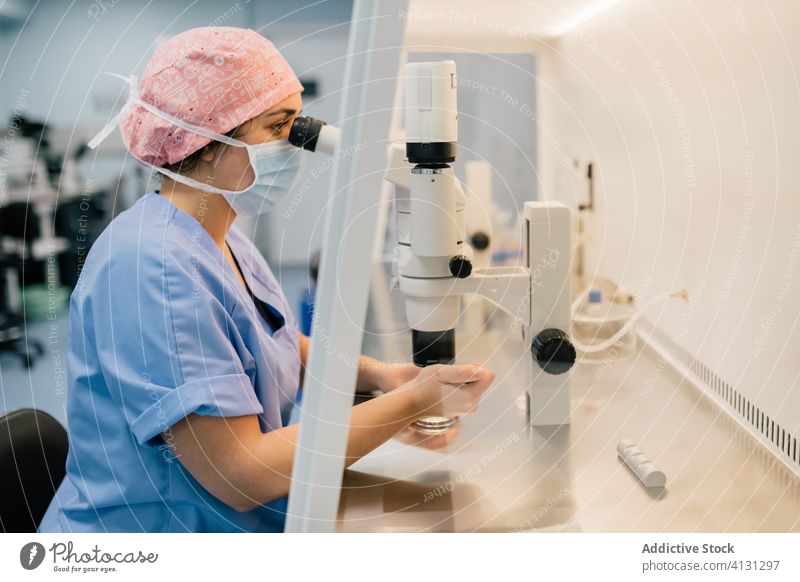Frau mit medizinischer Maske untersucht Eizelle durch Mikroskop Arzt untersuchen ovum Laborschale Klinik spritzen Uniform Mundschutz Embryo modern Medizin