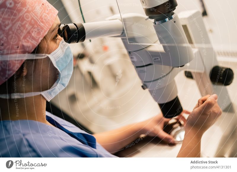 Frau mit medizinischer Maske untersucht Eizelle durch Mikroskop Arzt untersuchen ovum Laborschale Klinik spritzen Uniform Mundschutz Embryo modern Medizin