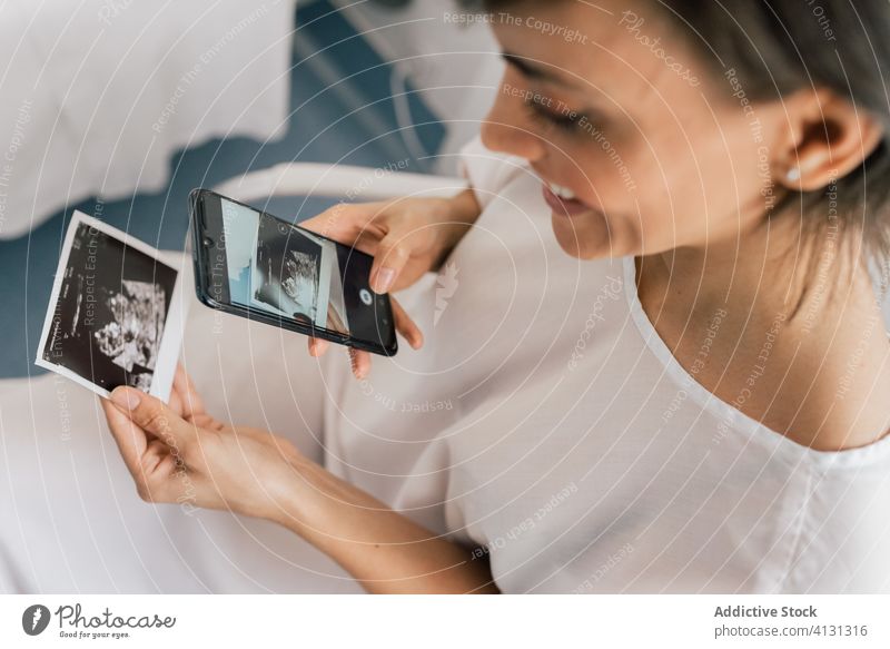 Glückliche schwangere Frau, die ein Foto von einer Ultraschalluntersuchung macht Sonogramm Scan fotografieren Schwangerschaft Lächeln Smartphone Station