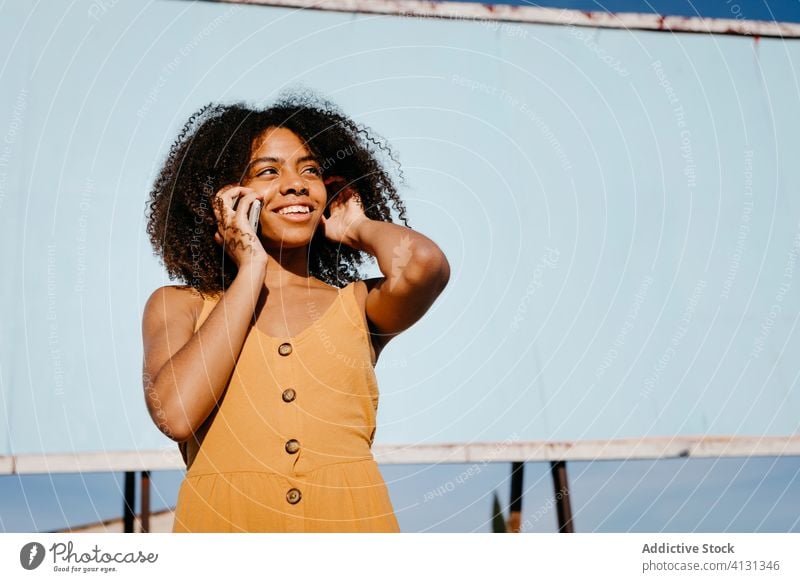 Junge zufriedene ethnische Frau benutzt Handy auf der Straße gegen leere große Tafel in einem Vorort Smartphone Plakatwand verwenden Freude Transparente