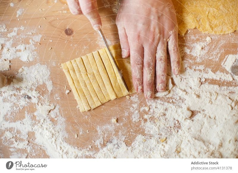 Unbekannte Person schneidet Nudelteig auf dem Tisch Teigwaren Spätzle selbstgemacht geschnitten Streifen Koch dünn Messer Mehl vorbereiten Küche rollen Prozess
