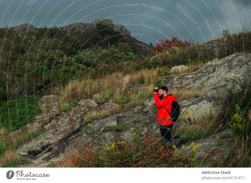 Männlicher Wanderer, der an einem bewölkten Tag auf einer Felsklippe steht und Fotos macht Mann Tourist Fotograf fotografieren Hügel Natur bedeckt trist