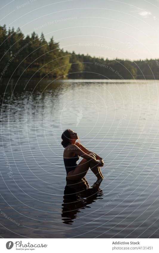 Frau im Badeanzug sitzt im See Wasser Windstille Sonnenuntergang genießen Sommer majestätisch sitzen Landschaft Wald ruhig Gelassenheit Harmonie friedlich