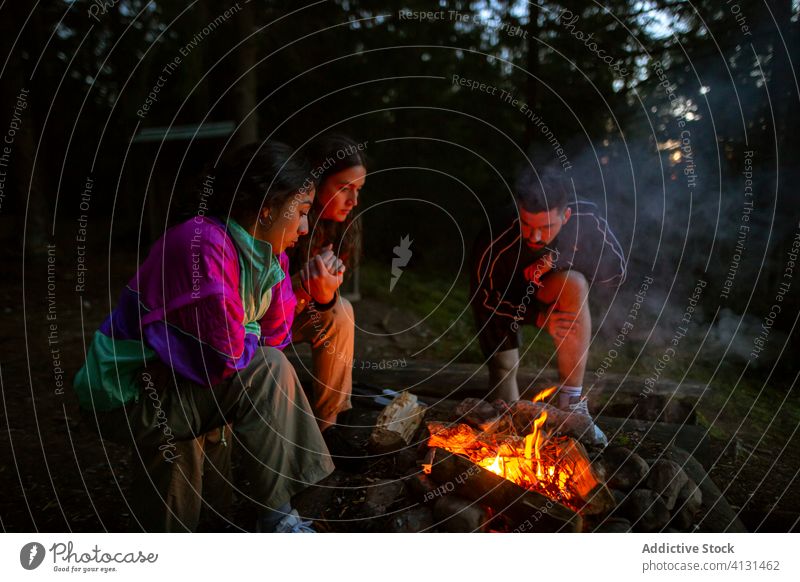 Gruppe multiethnischer Freunde am Lagerfeuer im Wald Menschengruppe sich[Akk] sammeln Freudenfeuer Wälder Aufwärmen Abend Unternehmen vielfältig