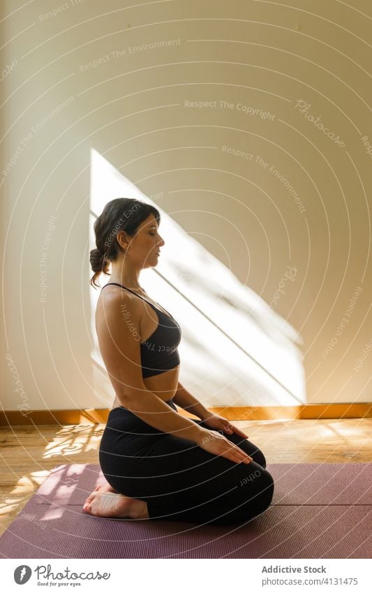 Ruhige Frau auf Matte sitzend in Diamantenpose zu Hause Yoga Karo-Pose Asana Unterlage Windstille meditieren Sonnenlicht Vajrasana schlank Athlet Denken