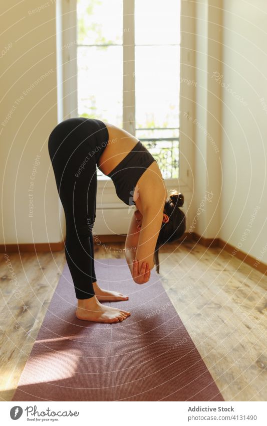 Unerkennbare Frau in Faltenwurf-Pose zu Hause im Sonnenlicht Yoga Appartement Windstille üben Asana Unterlage Energie Achtsamkeit Pose falten Barfuß