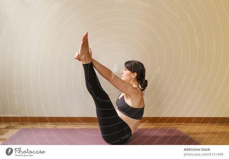 Flexible Frau in Bootspose sitzend beim Yoga-Workout üben Boot-Pose Dehnung Vitalität Füße berühren beweglich Gesunder Lebensstil Training Unterlage fokussiert