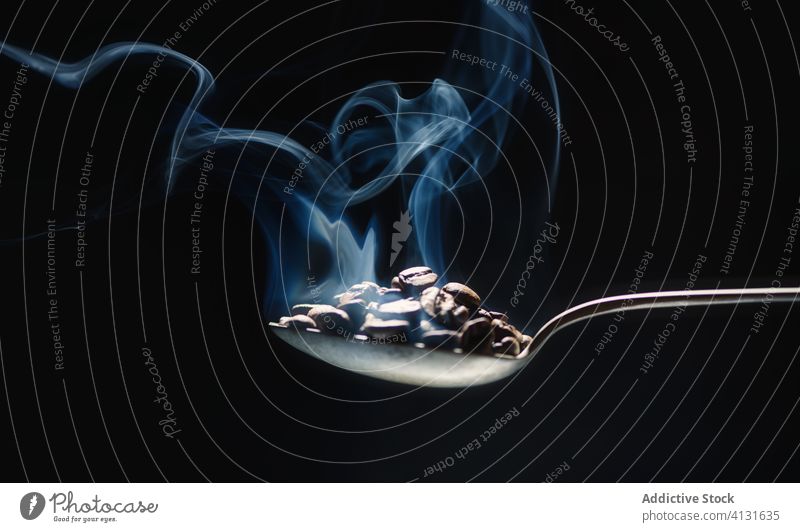 Metallischer Löffel mit frischen Kaffeekörnern auf schwarzem Hintergrund Ansicht Rauch Verdunstung nach oben Aroma dunkel Raum Energie Getränk Koffein lecker