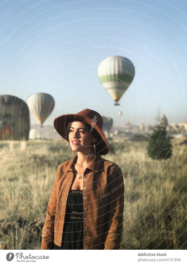 Reisende Frau vor dem Hintergrund von Heißluftballons im Feld Ballone reisen Tourist sonnig trendy Lächeln genießen Urlaub Feiertag Natur grün heiter sorgenfrei
