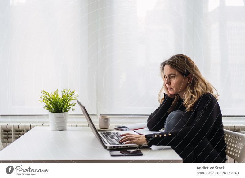 Entfernte Mitarbeiter, die zu Hause mit einem Laptop arbeiten Frau Arbeit heimwärts benutzend online abgelegen beschäftigt lässig ernst Tisch elektronisch