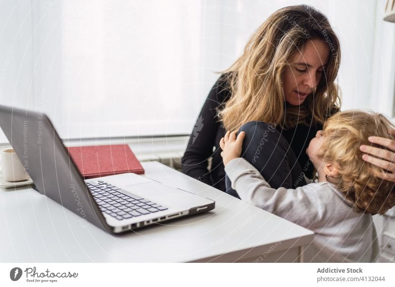 Beschäftigte Frau küsst Kind während Online-Arbeit zu Hause heimwärts Mutter Laptop abgelegen online Kuss Umarmung beschäftigt Umarmen Mutterschaft Komfort